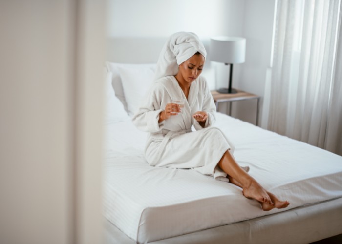 Frau in Bademantel nimmt Tabletten gegen eine Honeymoon Zystitis