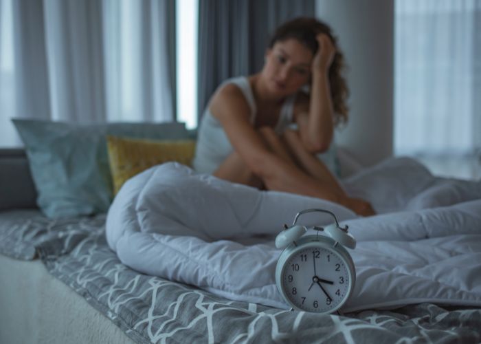 Frau sitzt gestresst im Bett - wenn Stress zu Schlafproblemen führt