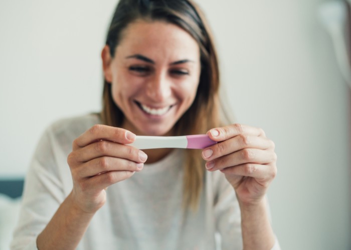 Frau hält Schwangerschaftstest in den Händen - Zusammenhang zwischen Unfruchtbarkeit und Scheidenflora
