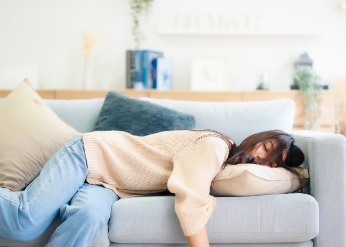 Schlafmangel - erschöpfte Frau liegt auf dem Sofa und versucht zu schlafen